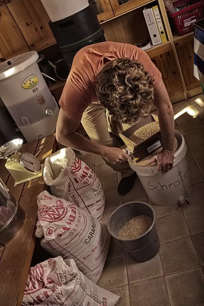 Ein Mann mit lockigem Haar mahlt konzentriert Malz für die Bierherstellung in einer handwerklichen Brauerei auf einer nordfriesischen Insel.