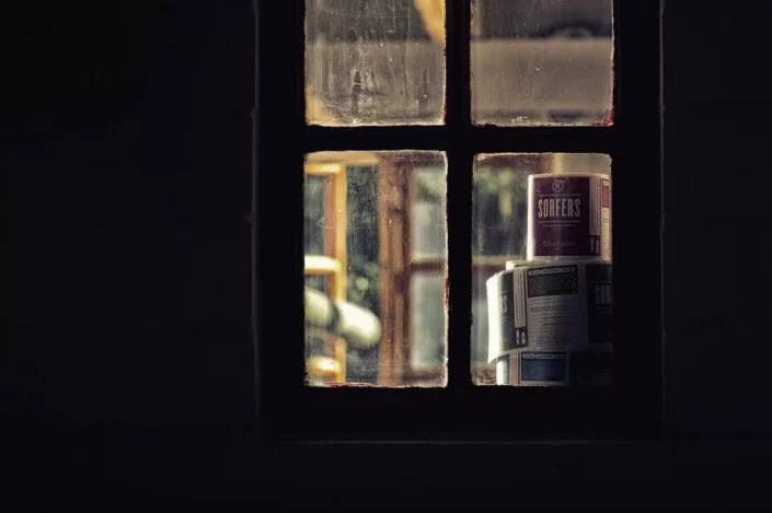 Ein stimmungsvoller Blick durch ein altes Sprossenfenster auf gestapelte Etiketten mit der Aufschrift SORFERS, eingefangen in warmem Licht.