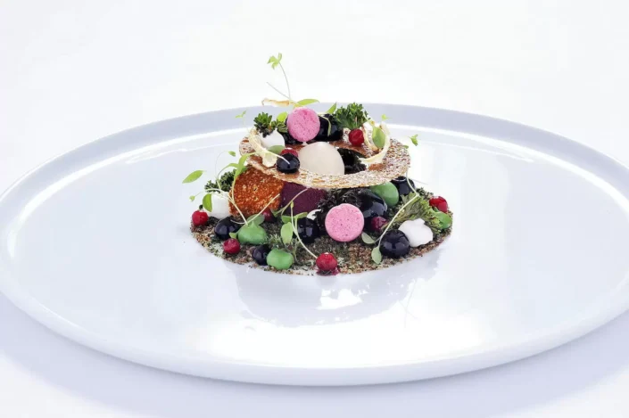Kunstvoll angerichtetes Dessert auf einem weißen Teller mit Beeren, feinen Cremes und knusprigem Gebäck, fotografiert für die Food Fotografie.