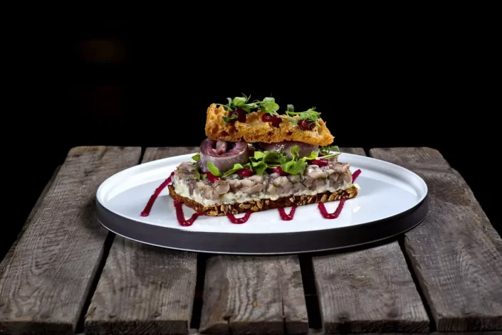 Ein kunstvoll angerichtetes Fischgericht auf dunklem Holz, serviert als kreative Foodfotografie für Sylter Gastronomiebetriebe.