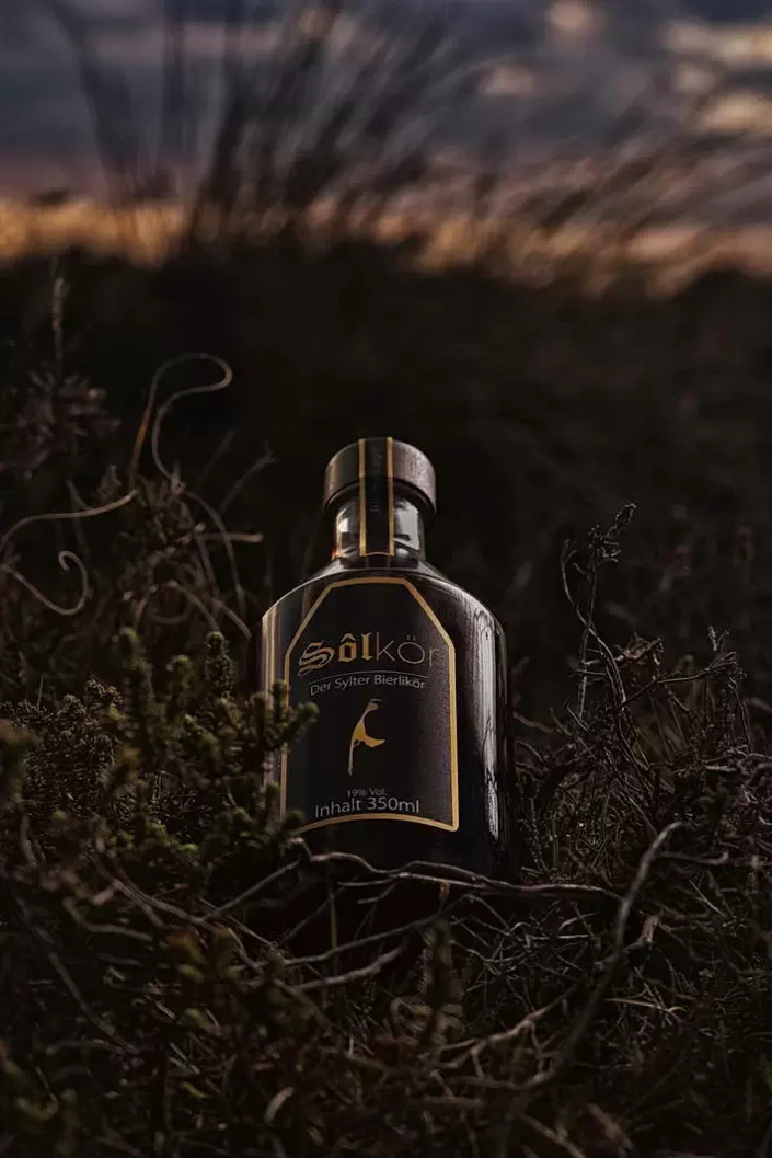 Eine Flasche Sölkör Sylter Bierlikör steht stimmungsvoll eingebettet in der dunklen, herbstlichen Heide-Landschaft der Insel Sylt.