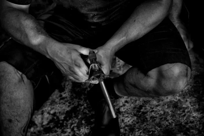 Schwarz-Weiß-Porträt der Hände eines Handwerkers, der konzentriert ein Werkzeug hält, im künstlerischen Stil der Insel-Fotografie.