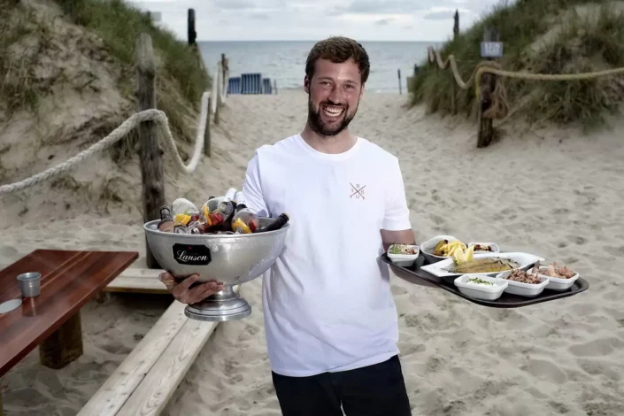 Ein lächelnder Kellner serviert am Strand von Sylt Getränke und Speisen für eine Veranstaltung, ideal für Event- und Hochzeitsfotografie.