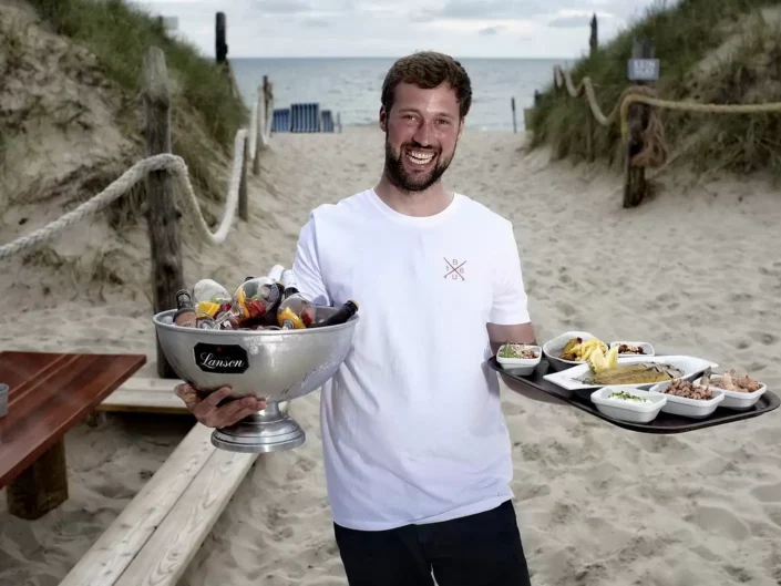 Ein lächelnder Kellner serviert am Strand von Sylt Getränke und Speisen für eine Veranstaltung, ideal für Event- und Hochzeitsfotografie.