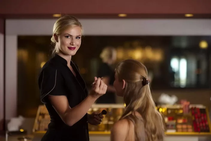 Eine Visagistin trägt bei der professionellen Hochzeitsfotografie auf Sylt Make-up auf, während die Braut geduldig im Hintergrund sitzt.