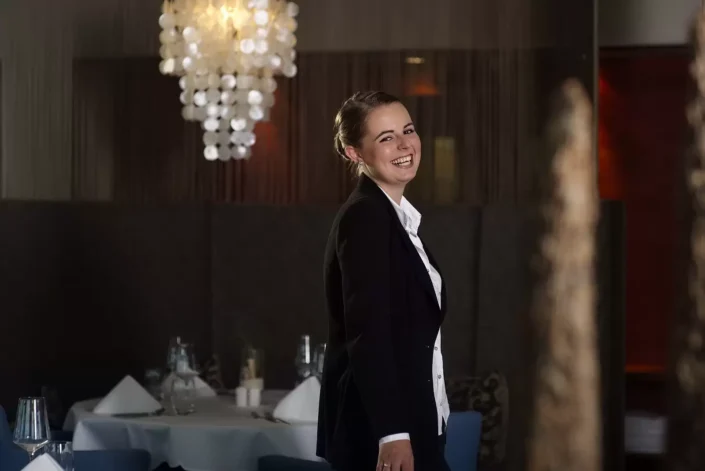 Eine junge Frau mit strahlendem Lächeln in einem eleganten schwarzen Blazer für ein professionelles Portrait auf Sylt, Amrum oder Föhr.
