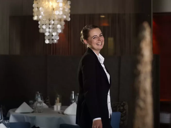 Eine junge Frau mit strahlendem Lächeln in einem eleganten schwarzen Blazer für ein professionelles Portrait auf Sylt, Amrum oder Föhr.