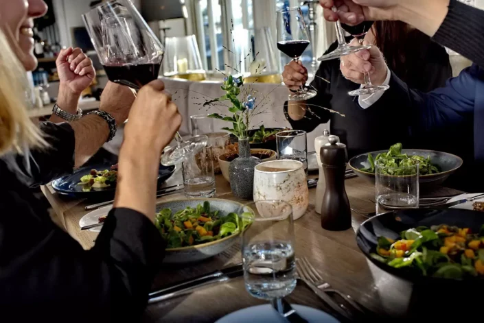 Eine Gruppe stößt bei einer Hochzeitsfeier auf Sylt mit Rotwein an, umgeben von festlich gedeckten Tischen und frischen Salaten.
