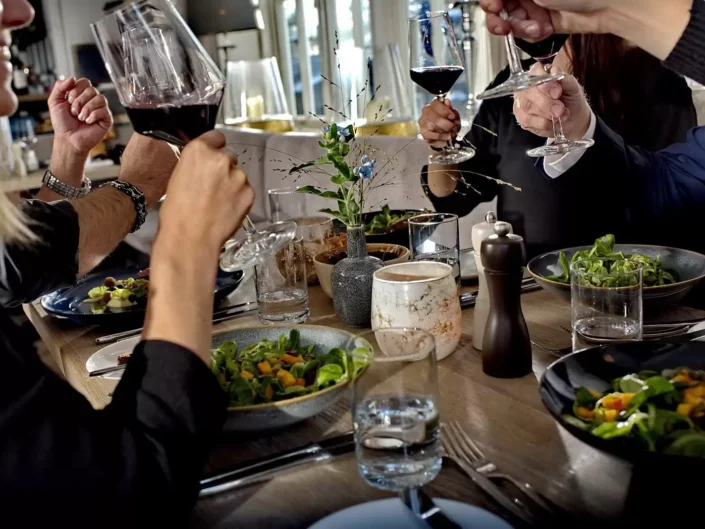 Eine Gruppe stößt bei einer Hochzeitsfeier auf Sylt mit Rotwein an, umgeben von festlich gedeckten Tischen und frischen Salaten.