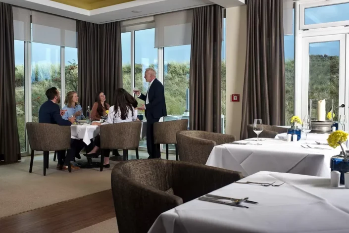Eine Gruppe genießt ein elegantes Abendessen in einem Restaurant mit Dünenblick, ideal für Hochzeitsfotografie auf Sylt, Amrum oder Föhr.