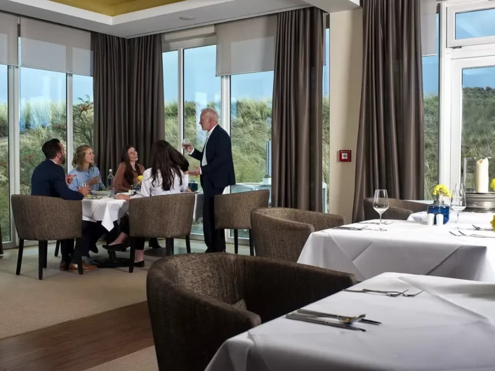 Eine Gruppe genießt ein elegantes Abendessen in einem Restaurant mit Dünenblick, ideal für Hochzeitsfotografie auf Sylt, Amrum oder Föhr.