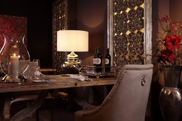 Ein luxuriös gedeckter Esstisch in einem eleganten Ambiente auf Sylt mit Kerzenlicht, Weinflaschen und kunstvollen Wandpaneelen im Hintergrund.
