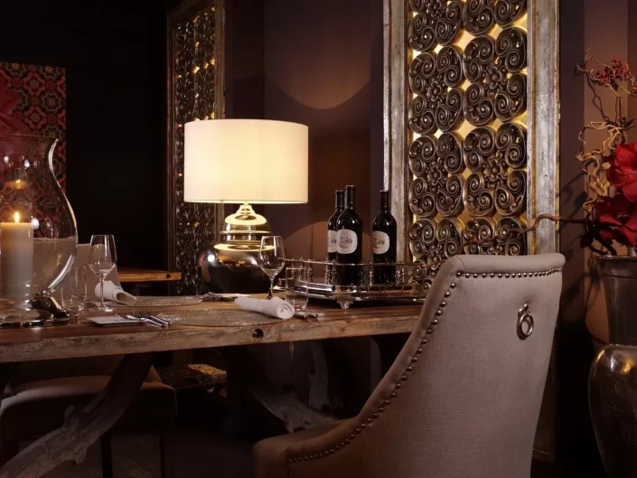 Ein luxuriös gedeckter Esstisch in einem eleganten Ambiente auf Sylt mit Kerzenlicht, Weinflaschen und kunstvollen Wandpaneelen im Hintergrund.