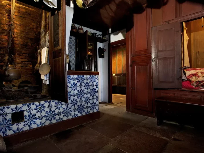 Historische Küche auf Sylt mit blau-weißen Kacheln, offenem Kamin und einer traditionellen Schrankbettnische in einem rustikalen Wohnraum.