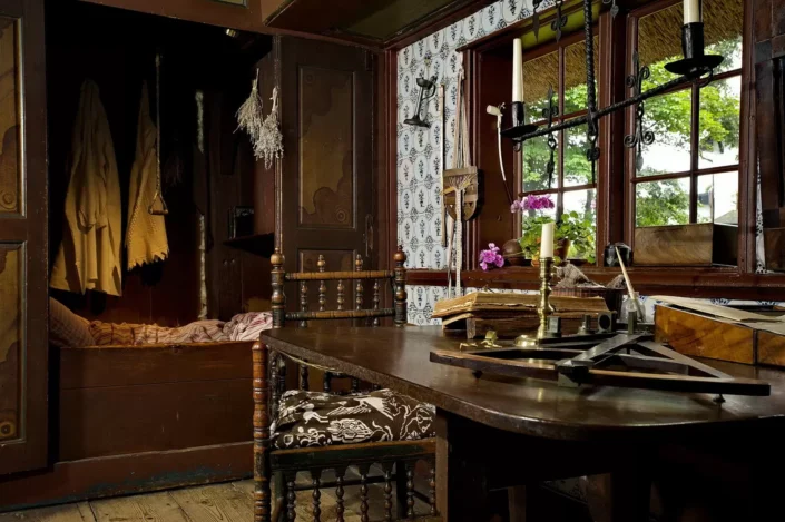 Historisches Interieur eines Sylter Friesenhauses mit Alkovenbett, dunklem Holztisch, antiken Stühlen und Blick durch das Fenster in den Garten.