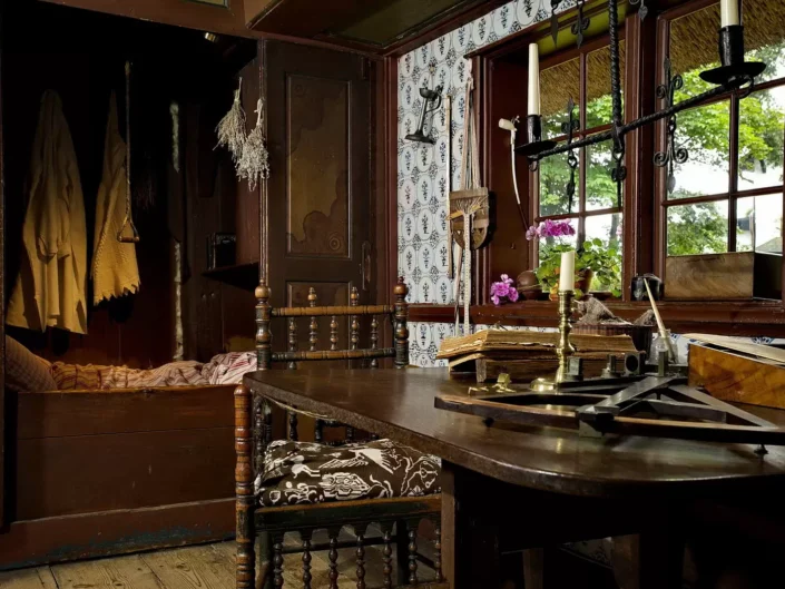 Historisches Interieur eines Sylter Friesenhauses mit Alkovenbett, dunklem Holztisch, antiken Stühlen und Blick durch das Fenster in den Garten.