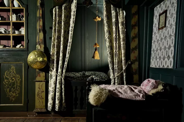 Historisches Schlafzimmer auf Sylt mit einer traditionellen Alkoven-Bettnische, gemusterten Vorhängen und einem antiken Schrank mit Porzellangeschirr.