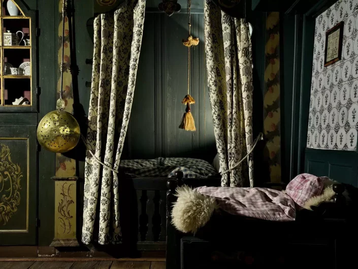 Historisches Schlafzimmer auf Sylt mit einer traditionellen Alkoven-Bettnische, gemusterten Vorhängen und einem antiken Schrank mit Porzellangeschirr.