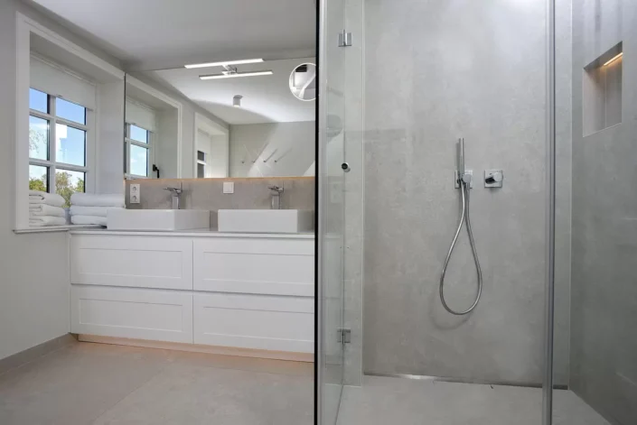 Modernes Badezimmer in einer Immobilie auf Sylt mit Doppelwaschtisch, großem Spiegel und einer begehbaren Dusche mit grauen Fliesen.