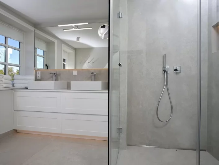Modernes Badezimmer in einer Immobilie auf Sylt mit Doppelwaschtisch, großem Spiegel und einer begehbaren Dusche mit grauen Fliesen.