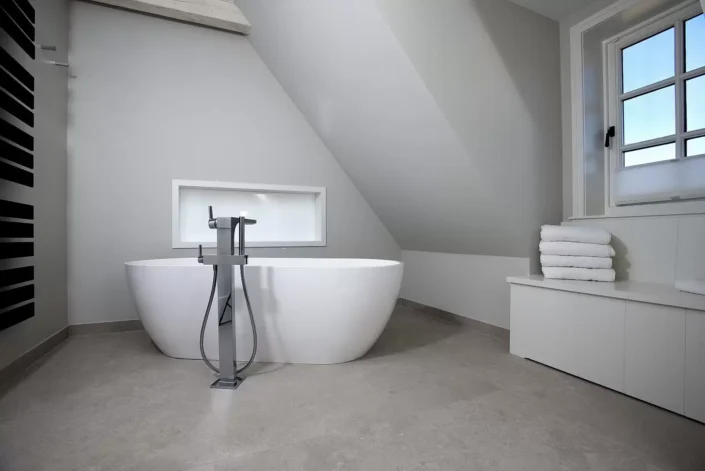 Modernes Badezimmer mit freistehender Badewanne, grauen Wänden und Dachschräge in einer exklusiven Immobilie auf Sylt.
