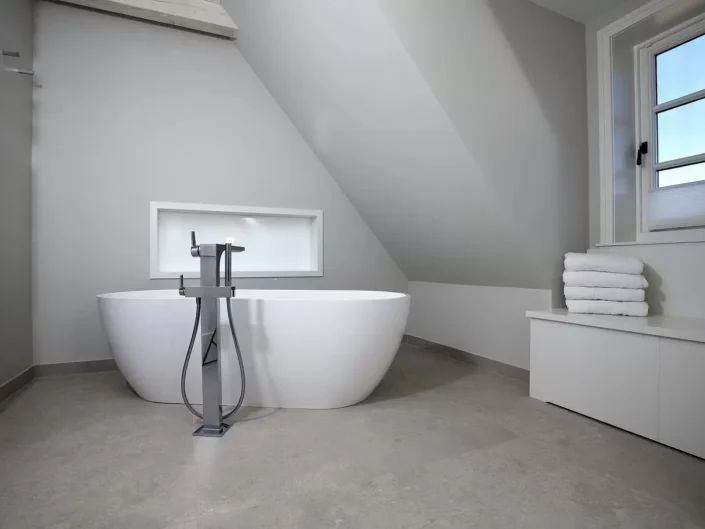 Modernes Badezimmer mit freistehender Badewanne, grauen Wänden und Dachschräge in einer exklusiven Immobilie auf Sylt.