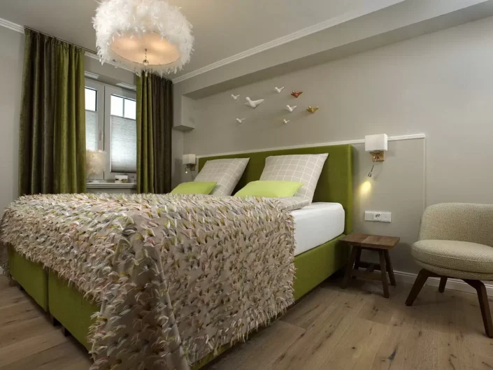 Modernes Schlafzimmer in einer Sylter Immobilie mit grünem Polsterbett, flauschiger Tagesdecke, Federlampe und dekorativen Vögeln an der Wand.