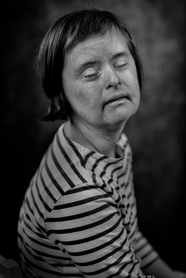Schwarz-Weiß-Porträt einer Frau mit Down-Syndrom, die entspannt die Augen geschlossen hat und ein gestreiftes Oberteil trägt, aufgenommen auf Sylt.