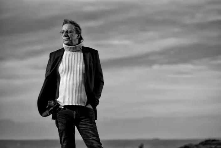 Schwarzweißaufnahme von amtierenden Bürgermeister von Westerland, Markus Gieppner, in Rollkragenpullover und Sakko, der nachdenklich in die Ferne blickt, aufgenommen in der Natur auf Sylt.