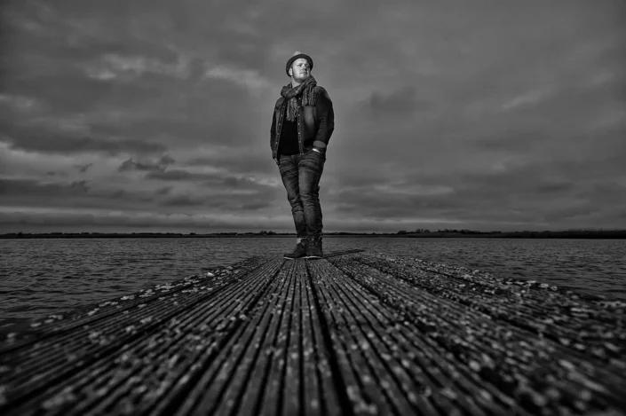 Stilvolles Schwarz-Weiß-Portrait eines Mannes auf einem Steg an der Nordsee, ein Ausdruck künstlerischer Portraitfotografie auf den Inseln.
