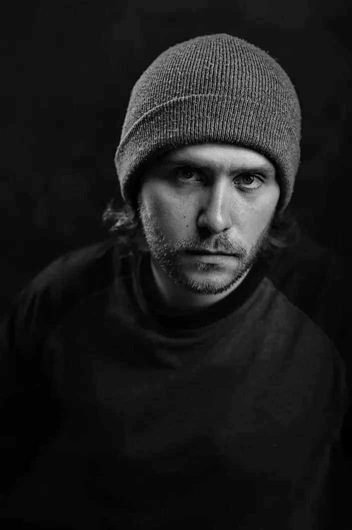 Schwarz-Weiß-Portrait eines Mannes mit Mütze vor dunklem Hintergrund, ausdrucksstarke Fotografie für authentische Portraits auf den Inseln.