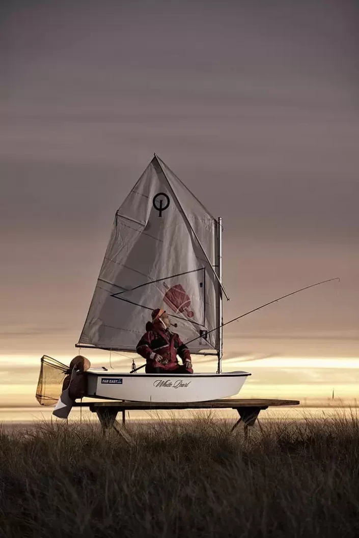 Ein kunstvolles Portrait auf Sylt: Ein Angler in einem Segelboot namens White Pearl vor stimmungsvoller Küstenkulisse bei Sonnenuntergang.