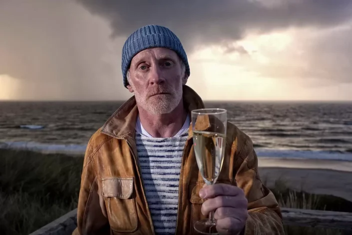 Stilvolles Portrait eines Mannes mit Champagnerglas vor der dramatischen Nordseekulisse, eingefangen durch exklusive Insel-Fotografie.