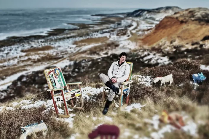 Ein Mann sitzt in einem künstlerischen Stuhl auf einer verschneiten Düne bei Sylt – ein stimmungsvolles Portrait für exklusive Fotografie.