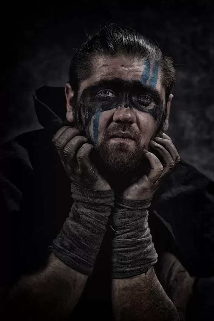 Ein ausdrucksstarkes, künstlerisches Portrait von Bassisten von der Band Sagenbringer mit dunkler Kriegsbemalung, das die Tiefe professioneller Portraits unterstreicht.