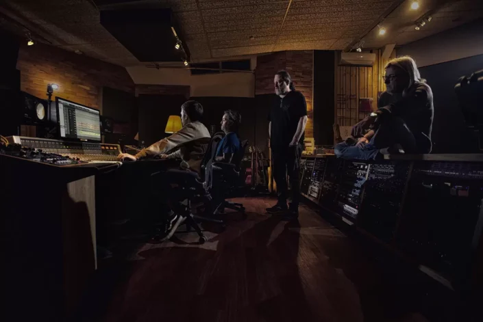 Vier Männer arbeiten konzentriert in einem stimmungsvoll beleuchteten Tonstudio an einem Mischpult und Computer. Foto von Fotografen Sylt.