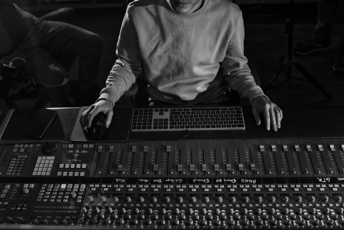 Ein Tontechniker arbeitet konzentriert an einem großen Mischpult in einem dunklen Studio, die Hände ruhen auf der Maus und dem Keyboard.