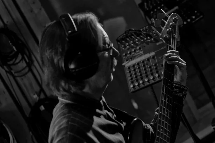 Ein Musiker mit Kopfhörern spielt konzentriert E-Bass in einem Tonstudio in Hamburg, eingefangen in einer stimmungsvollen Schwarz-Weiß-Aufnahme von Fotografen Sylt.