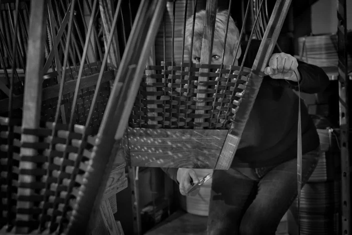 Eine konzentrierte Handwerkerin flicht in einer Werkstatt mit viel Hingabe einen Korb, aufgenommen vom Fotografen Sylt in Schwarz-Weiß.