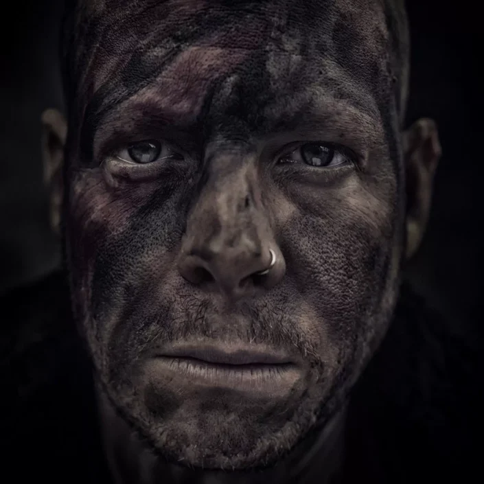Nahaufnahme eines Mannes mit schmutzverschmiertem Gesicht und Nasenpiercing, aufgenommen in einem ausdrucksstarken Portrait auf Sylt.