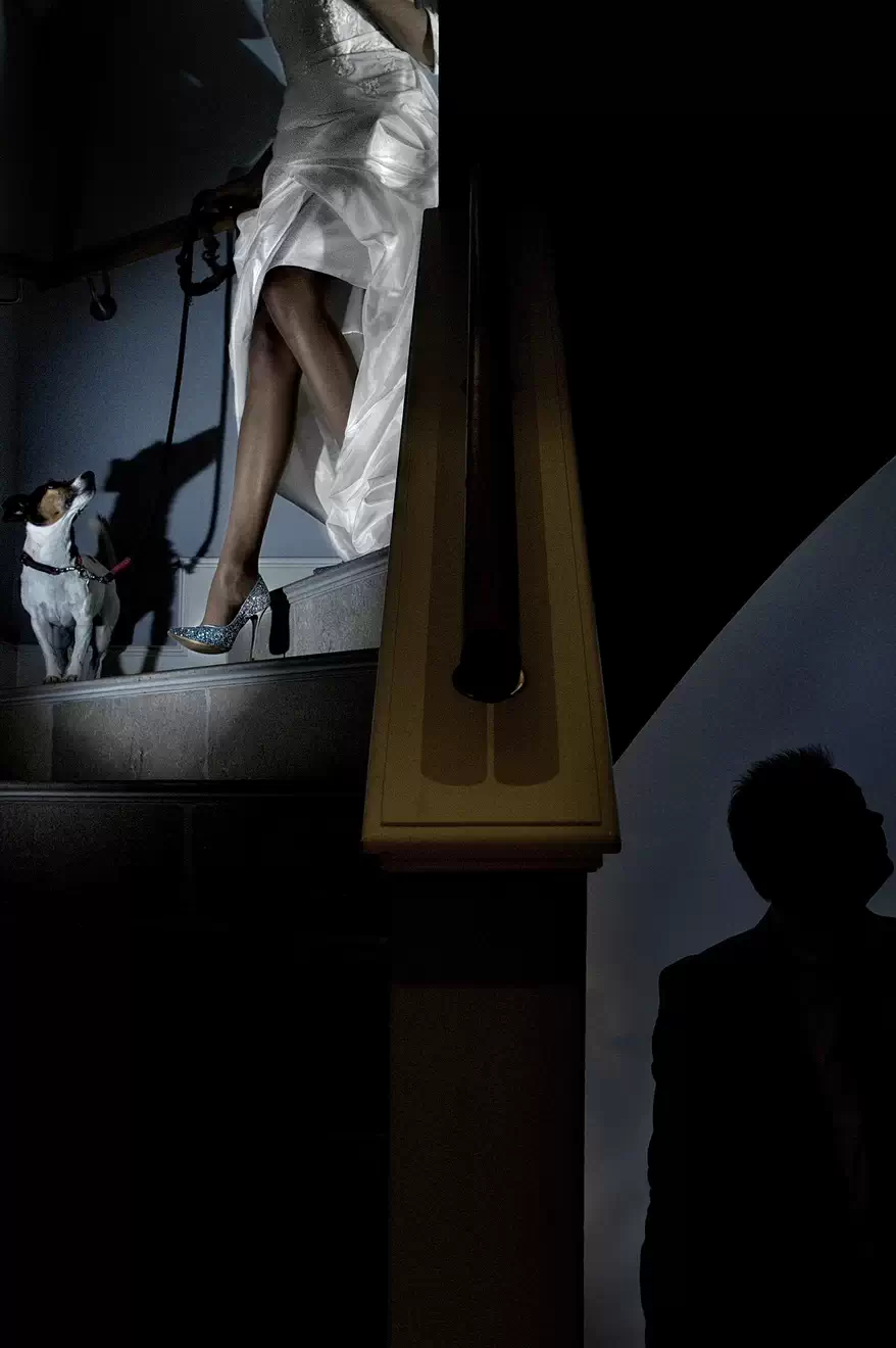 Eine Braut in einem weißen Kleid und glitzernden High Heels geht eine Treppe in einer exklusiven Immobilie auf Sylt hinunter, begleitet von einem Hund.