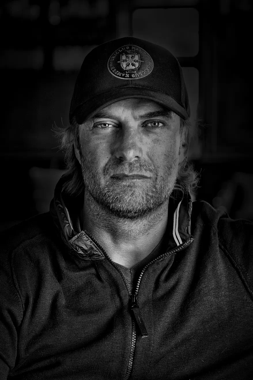 Schwarz-Weiß-Porträt von Juergen Klopp, der eine Baseballkappe mit dem Logo des Skiclub Kampen auf Sylt trägt und direkt in die Kamera blickt.